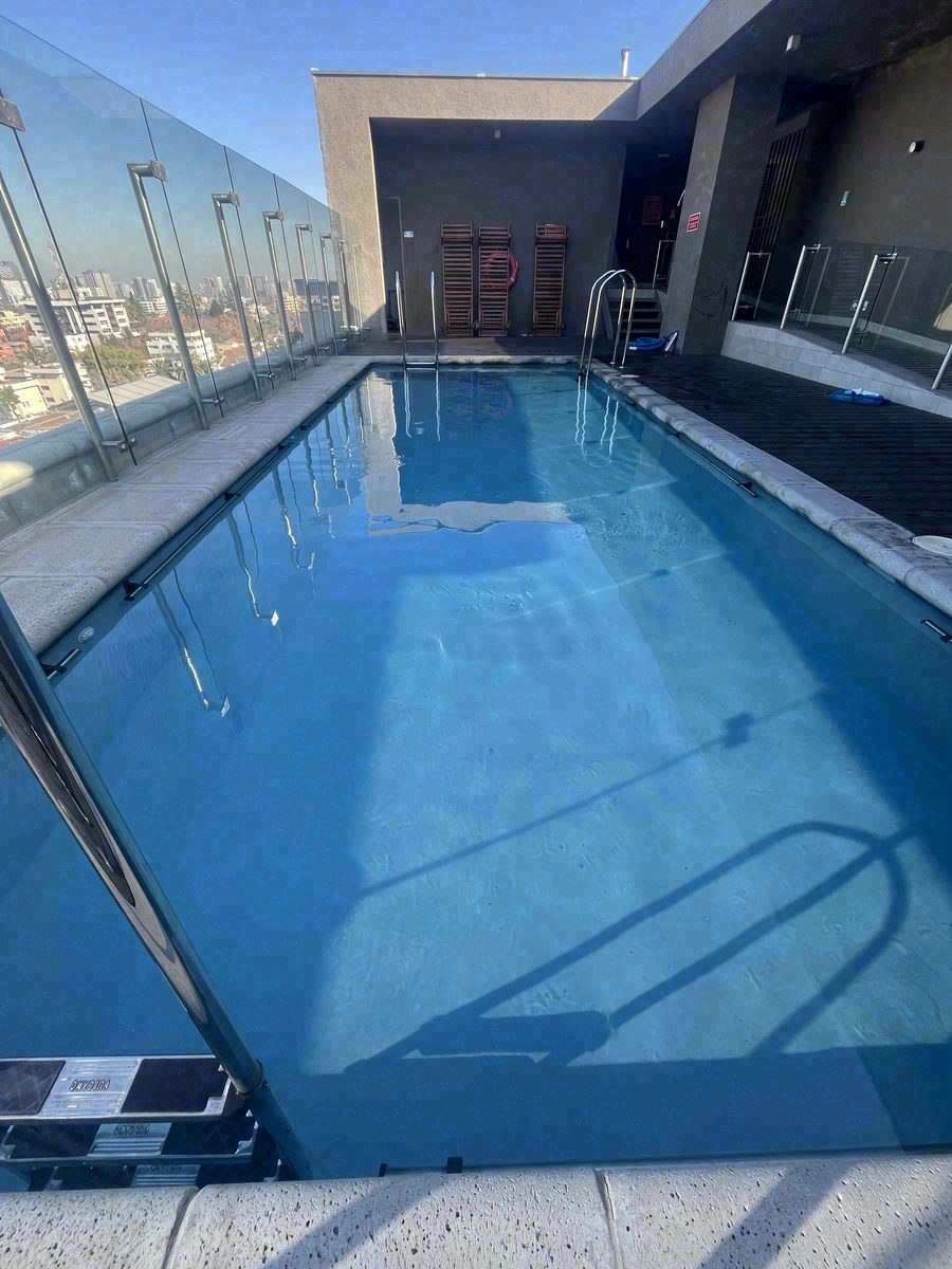 Piscina de largo en azotea con baranda de vidrio y vista a la ciudad