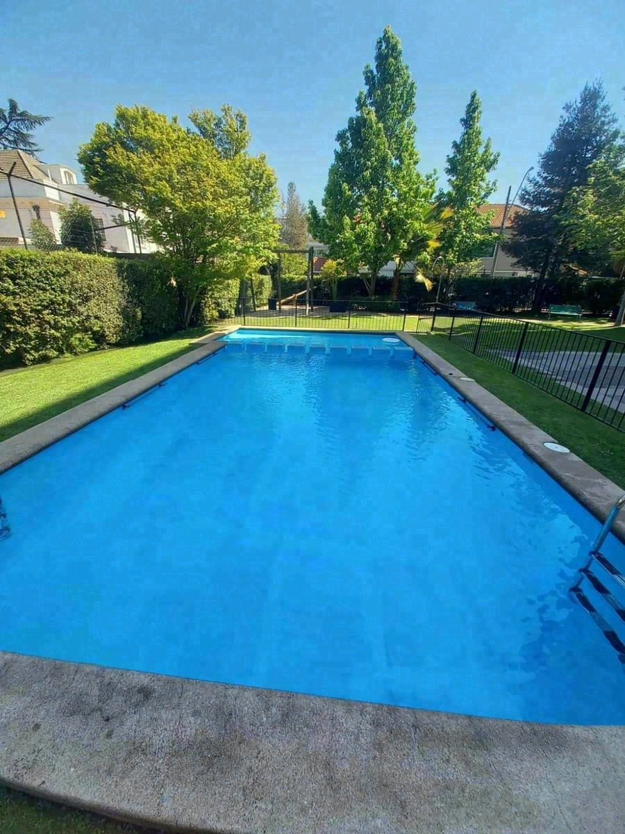 Piscina de condominio rodeada de jardín y árboles